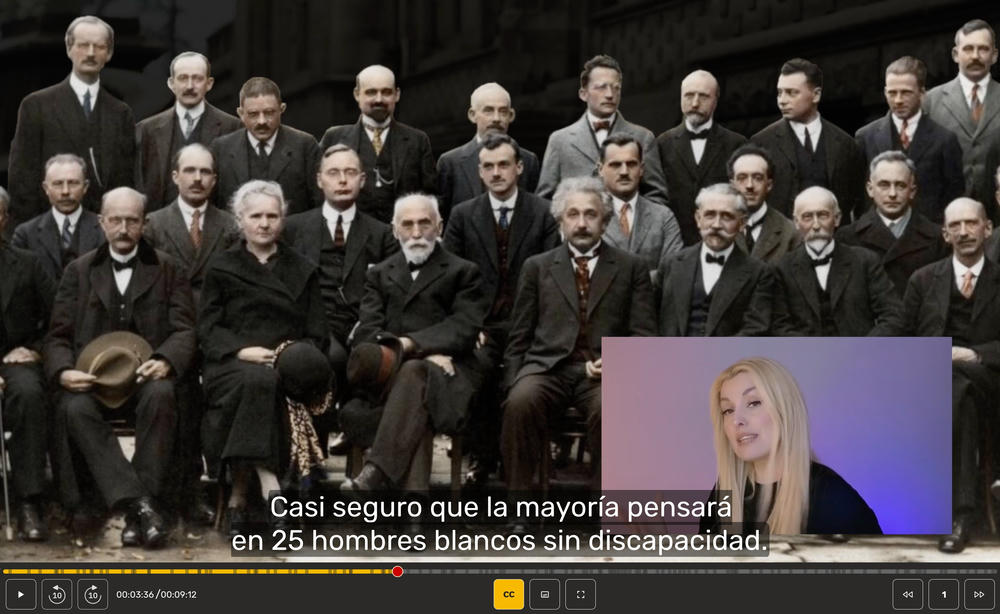 En pantalla, foto histórica del V Congreso Solvay de 1927: unas treinta personas posan, con apariencia seria, en tres filas ante el antiguo Instituto Solvay de Fisiología. Entre ellas, Madame Curie. El subtítulo dice: «Casi seguro que la mayoría pensará en 25 hombres blancos sin discapacidad.»